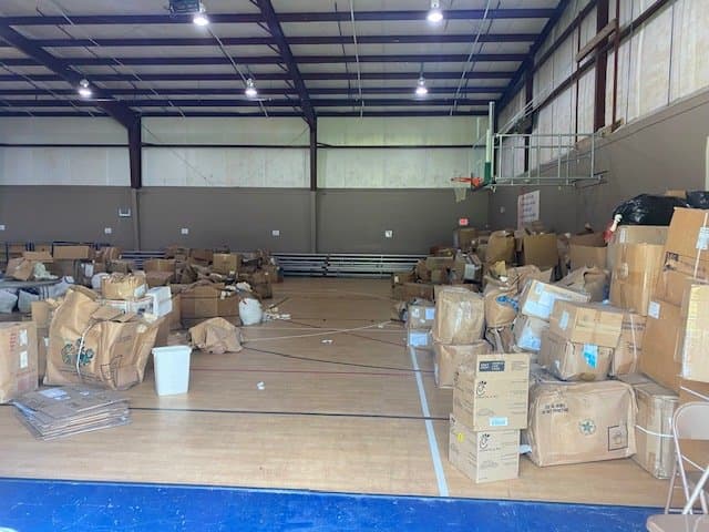 An indoor gymnasium filled with numerous cardboard boxes and packages scattered across the floor.