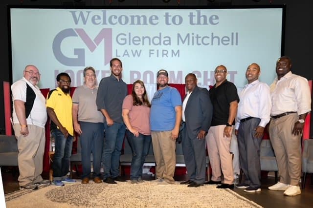 Group of ten people standing in front of a screen displaying a welcome message for Glenda Mitchell Law Firm.